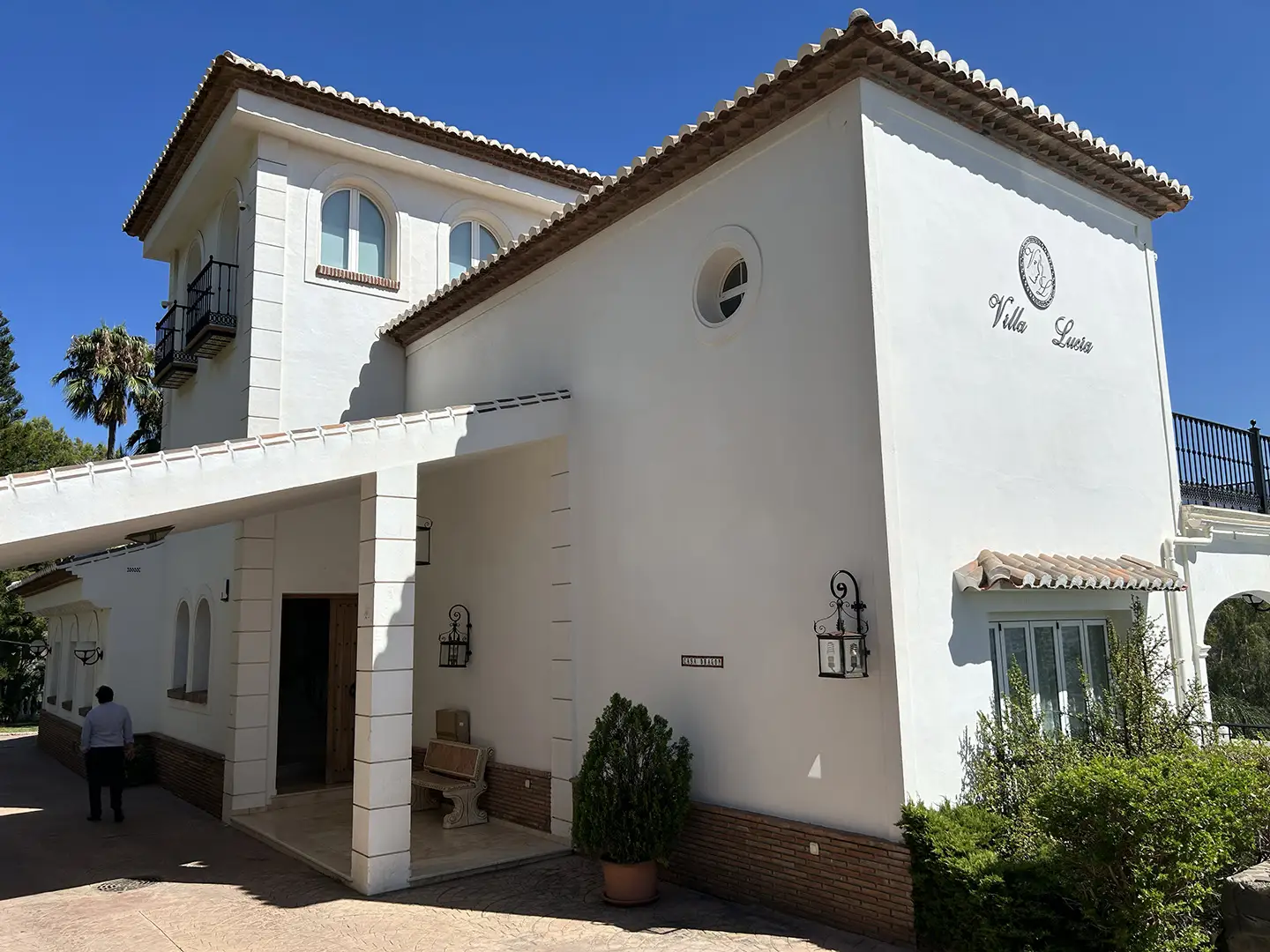 Белый фасад дома с башней, входной дверью и табличкой Villa Lucia.